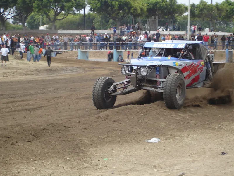 Race buggy kicks up dirt in front of fans behind a fence at the 2007 Baja 500