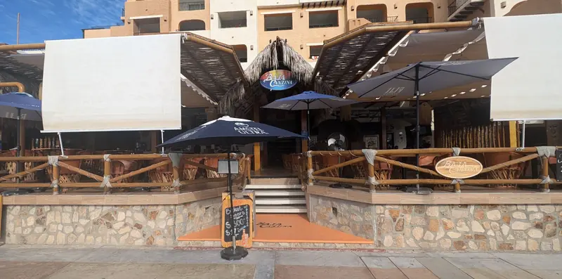 Front of Baja Cantina in Cabo San Lucas, with its palapa roof, white awnings and steps up from the marina walk