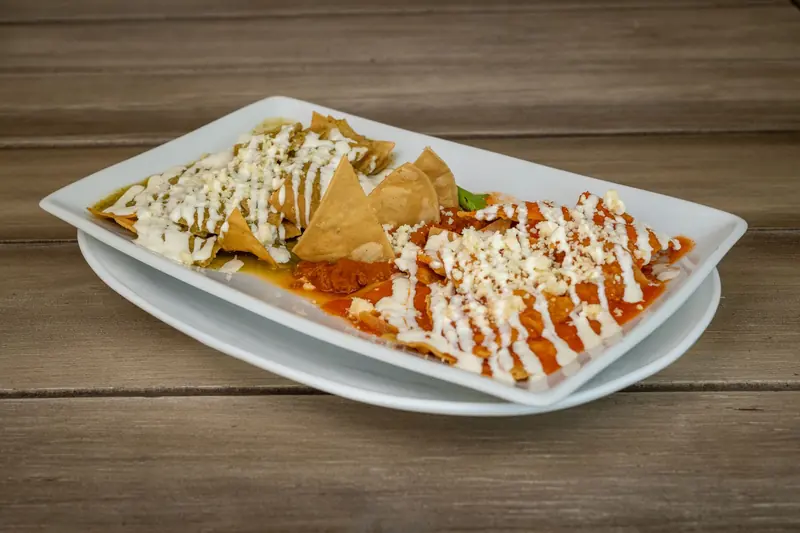 Plato de chilaquiles con salsa roja y verde, crema y queso sobre una mesa de madera