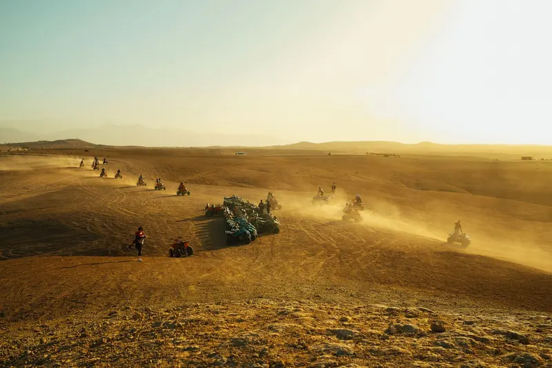 A group of riders on quad bikes crossing open sandy desert terrain at sunset