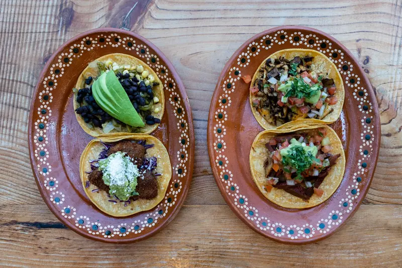 Tacos with avocado and salsa on two brown clay plates on a wooden table