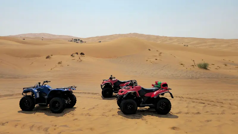 Three ATVs parked on a sand dune under a clear sky