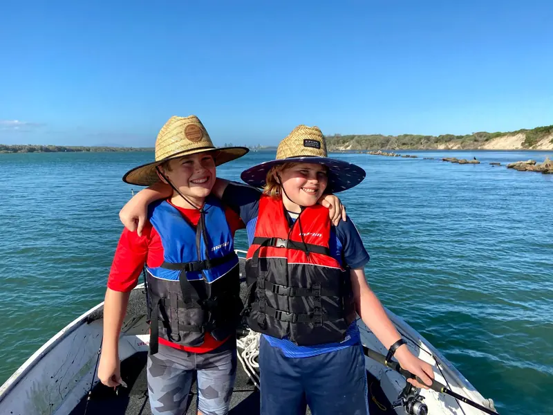 Two smiling kids in life jackets and straw hats on a boat on a sunny day