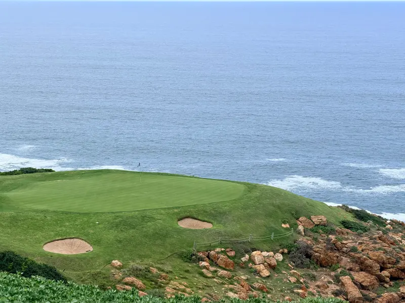 A golf green with two sand bunkers on a grassy bluff above the ocean