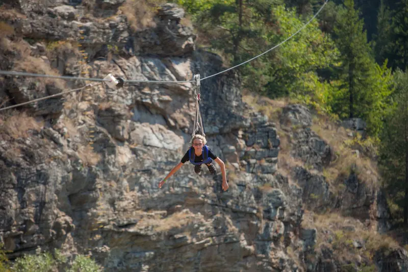 A person in a harness ziplining across a rocky canyon on a sunny day