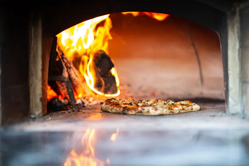 Pizza horneándose en un horno de leña de ladrillo con el fuego al fondo