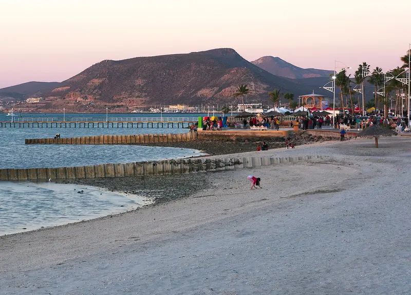 Malecón de La Paz al atardecer con gente junto al kiosco y el cerro al fondo