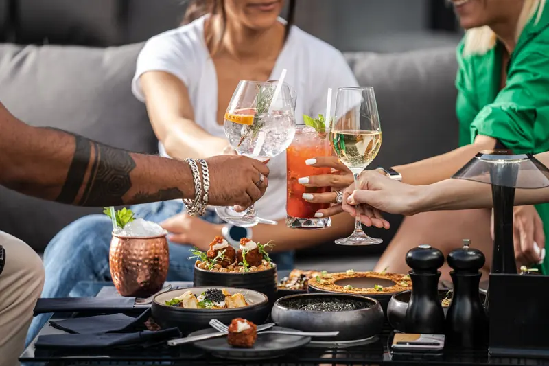 Colleagues clinking cocktail glasses over a table of food at an outdoor gathering