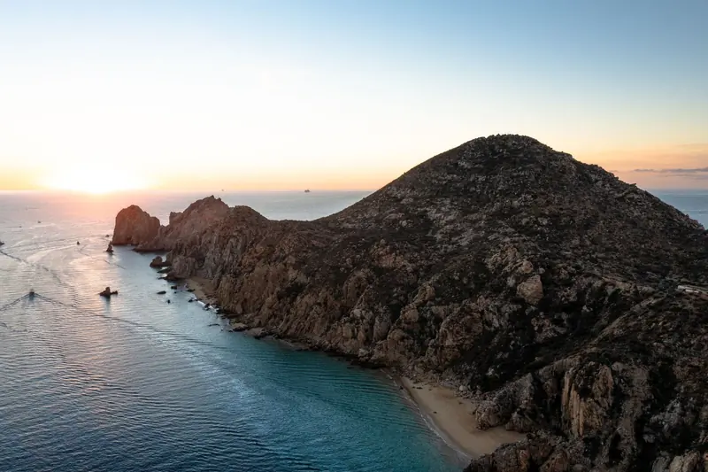 The sun setting over the Pacific beyond the rocky ridge of Land's End, with boats near the shore