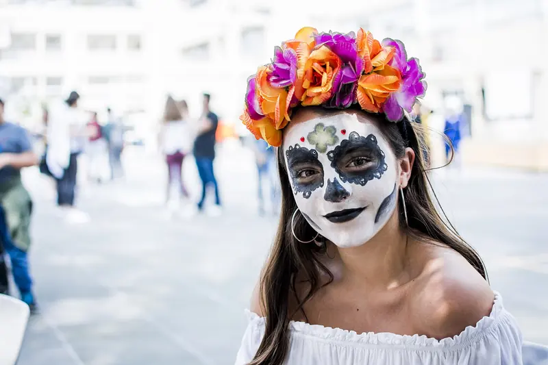 Young woman in catrina face paint with an orange and purple flower crown at a festival in Mexico