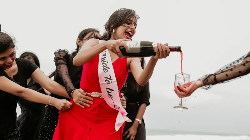 Novia con banda de bride to be sirviendo champaña entre sus amigas, todas riendo
