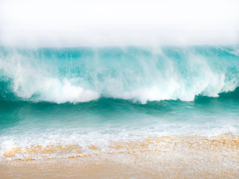 A big turquoise wave breaking on a sandy beach near Cabo San Lucas