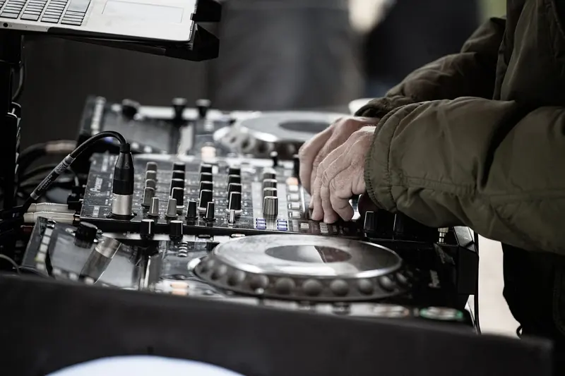 A DJ's hands on a mixer and turntable at an outdoor daytime set
