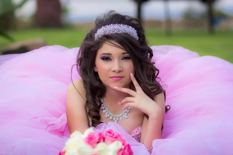 Quinceañera con vestido rosa de gala y tiara posando al aire libre
