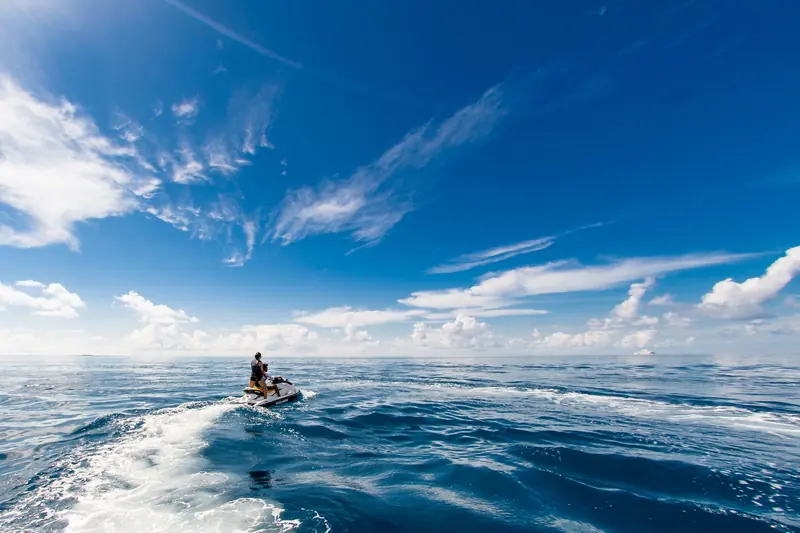 A rider on a jet ski leaving a white wake on blue open water