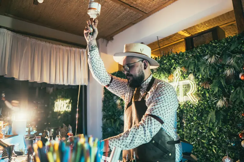 Bartender con sombrero sirviendo cocteles en una barra iluminada de noche