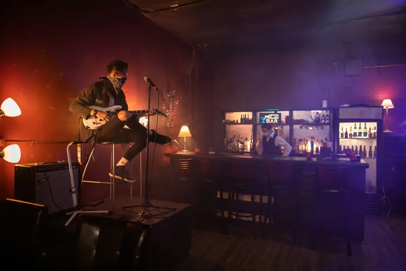 Un músico toca la guitarra en un bar con luz baja y botellas al fondo
