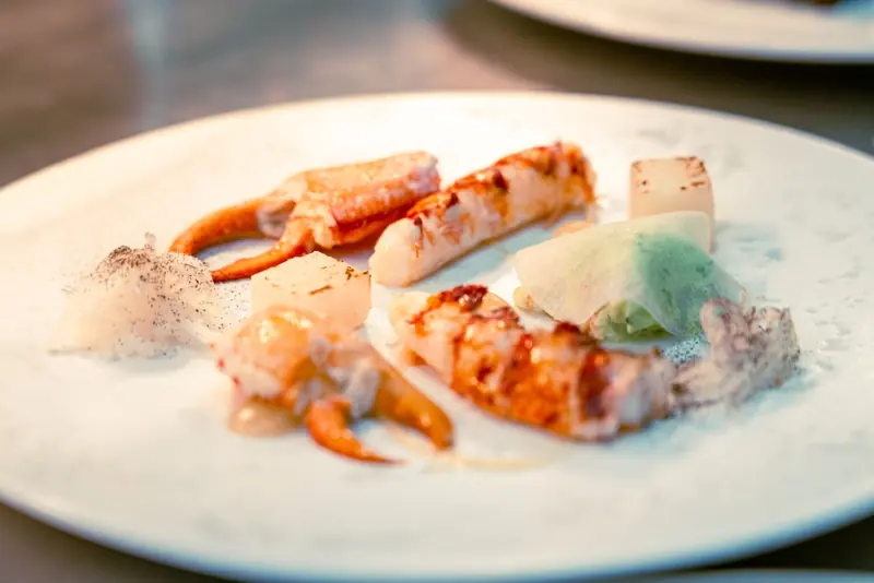 Lobster and crab claws plated with foam and herbs on a white dinner plate