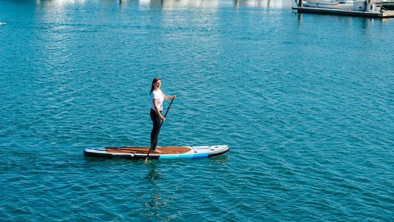 A woman standing on a paddle board on flat blue water
