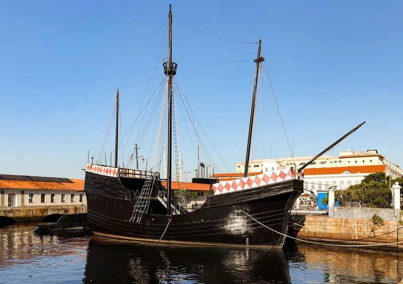 A black wooden sailing ship with tall masts moored in a calm harbor
