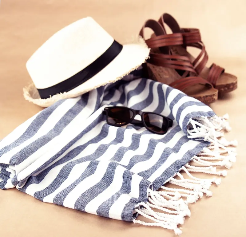 Un sombrero de paja, una toalla de rayas, lentes de sol y sandalias sobre un fondo claro