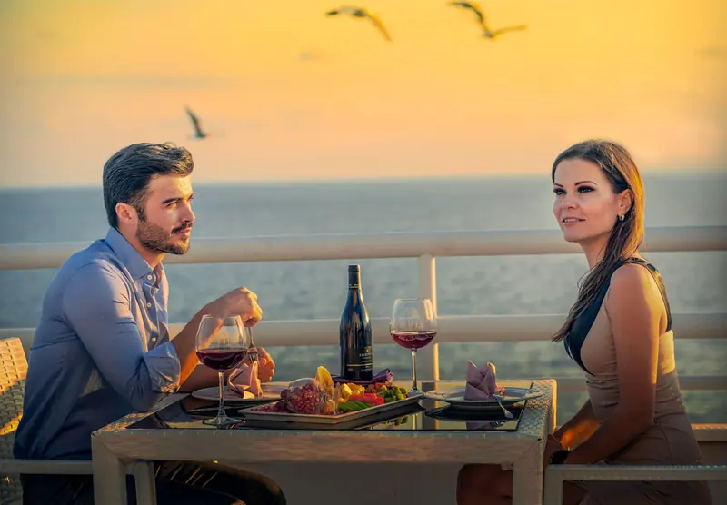 A couple at a table with wine at sunset overlooking the ocean