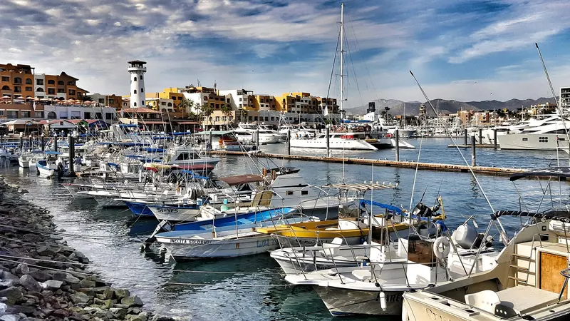 Yachts and pangas in the Cabo San Lucas marina with the lighthouse and waterfront buildings behind