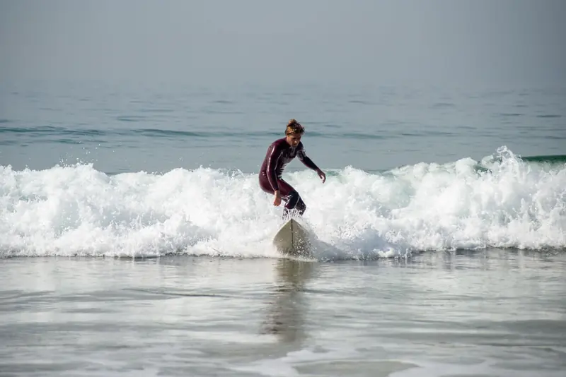 A surfer in a wetsuit standing on a board in small whitewater near shore