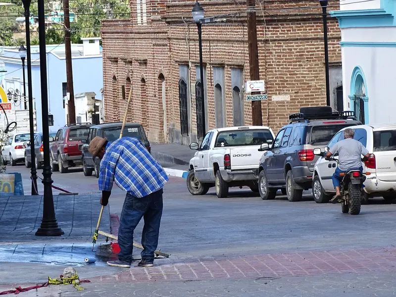 Calle del centro de Todos Santos con edificios de ladrillo, autos estacionados y un hombre barriendo la banqueta