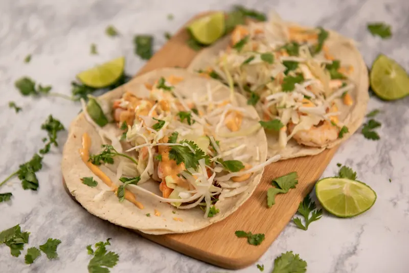 Shrimp tacos with shredded cabbage and cilantro on a wooden board, lime halves around them