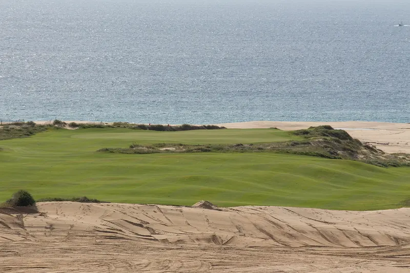 A green on the Dunes Course at Diamante with sand dunes in front and the Pacific behind