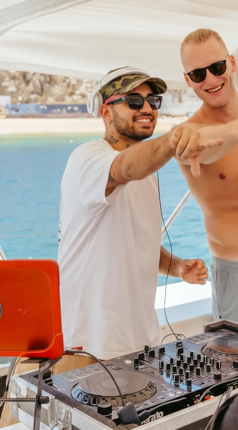DJ Basneit at his controller on a yacht in Cabo, pointing at a guest, with the beach behind