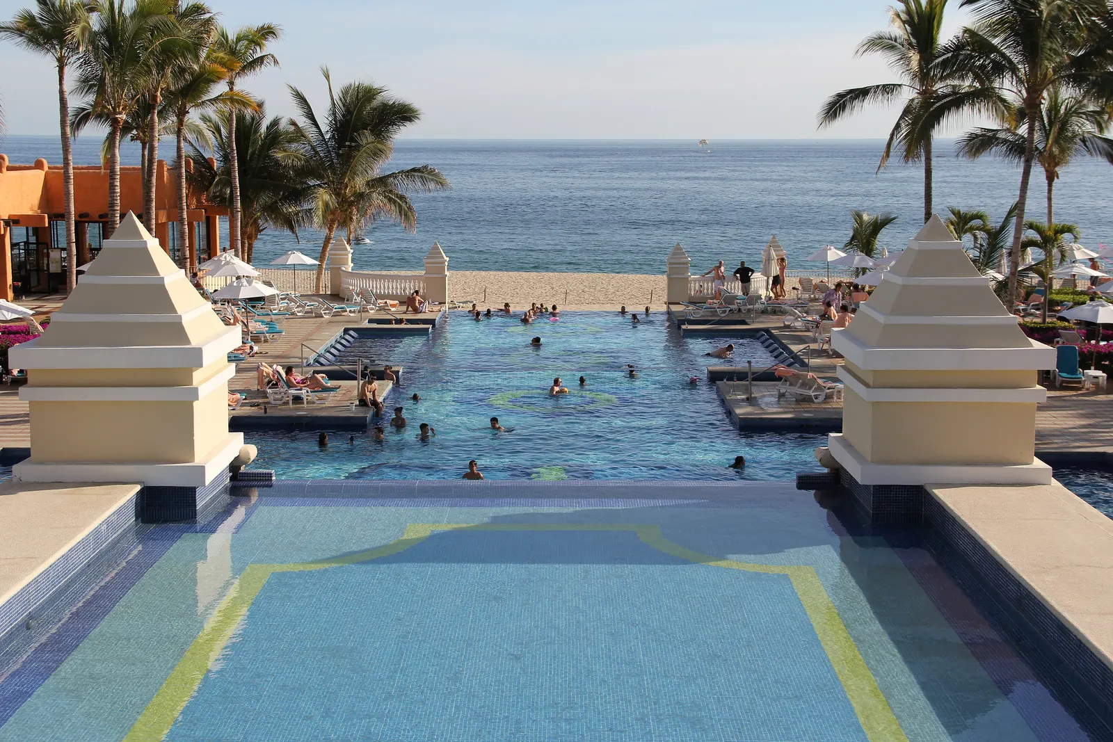 The long pool of the Riu Palace Cabo San Lucas running toward the beach, with palms on both sides