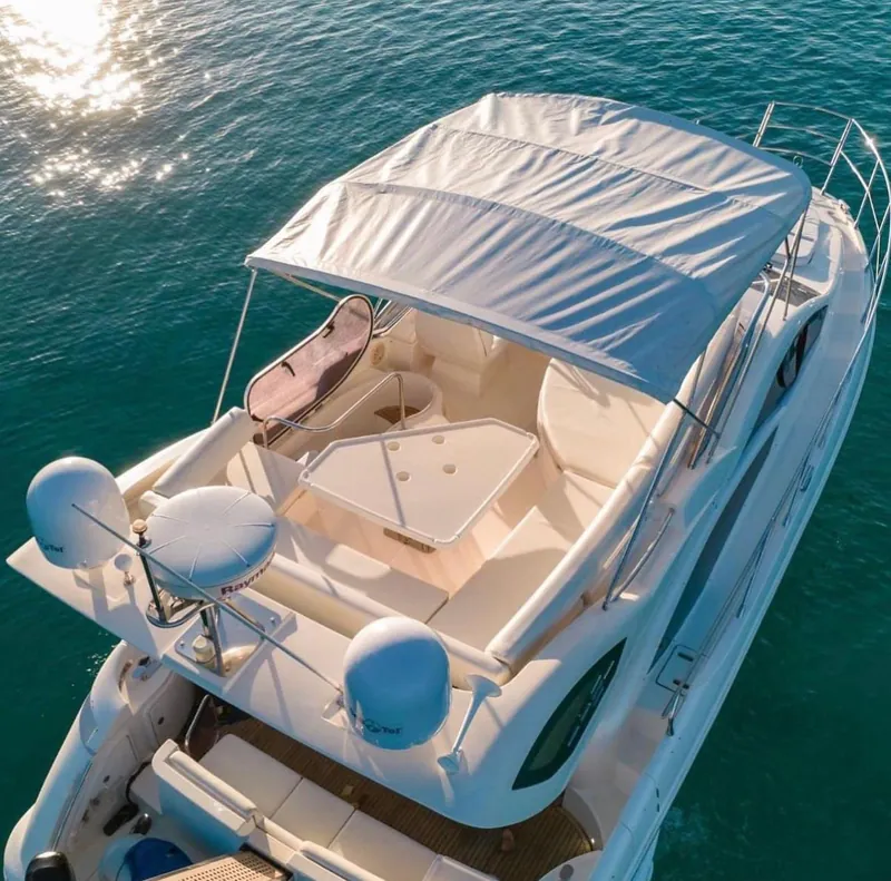 The flybridge of the Azimut 45, shaded by its bimini, with an L-shaped lounge, table and sunpad