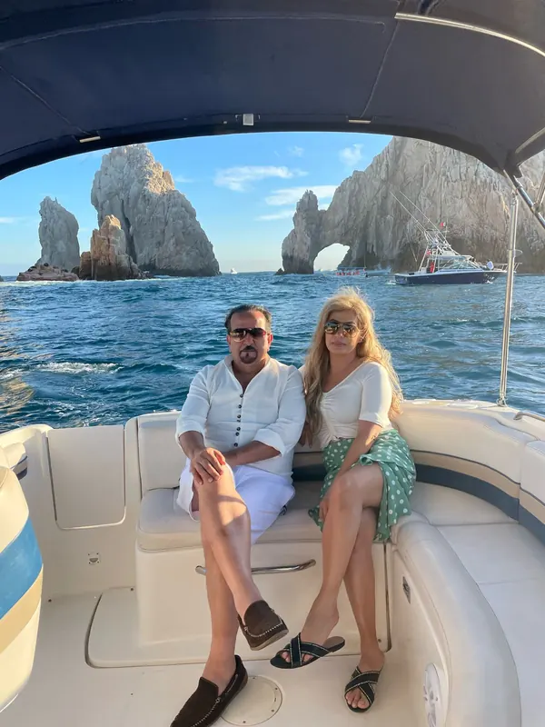 Two guests sitting under the shade top of the Chaparral 28 with the Arch and the rocks of Land's End behind them