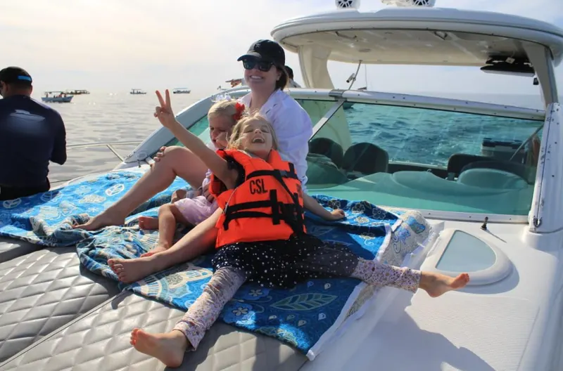 Child in a life jacket sitting on the floating mat beside the Maxum 45