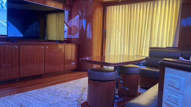 Salón del McKinna 70 con televisión, muebles de madera y mesa con dos taburetes